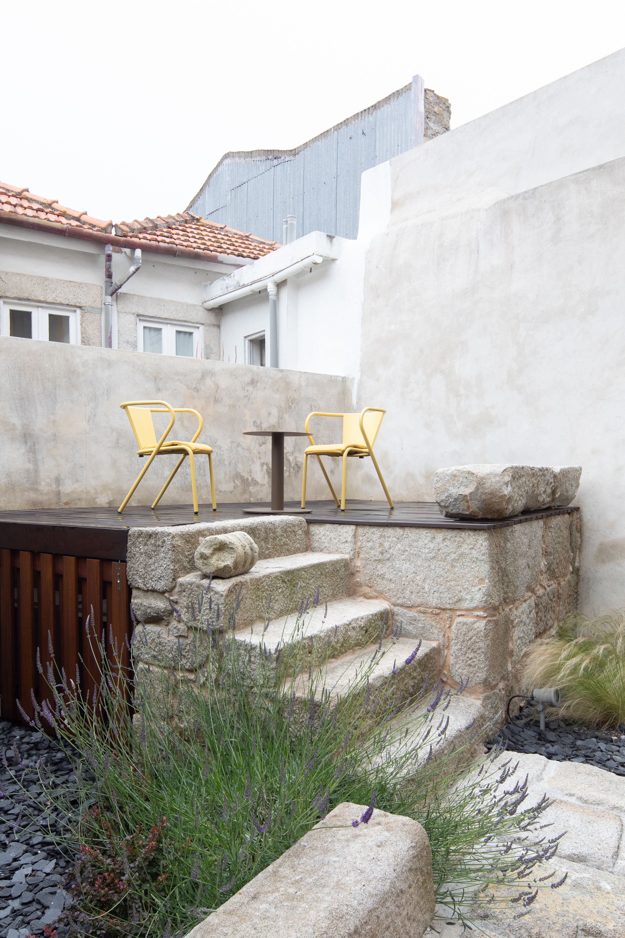 A patio with two yellow chairs and a table, surrounded by stone steps and plants.