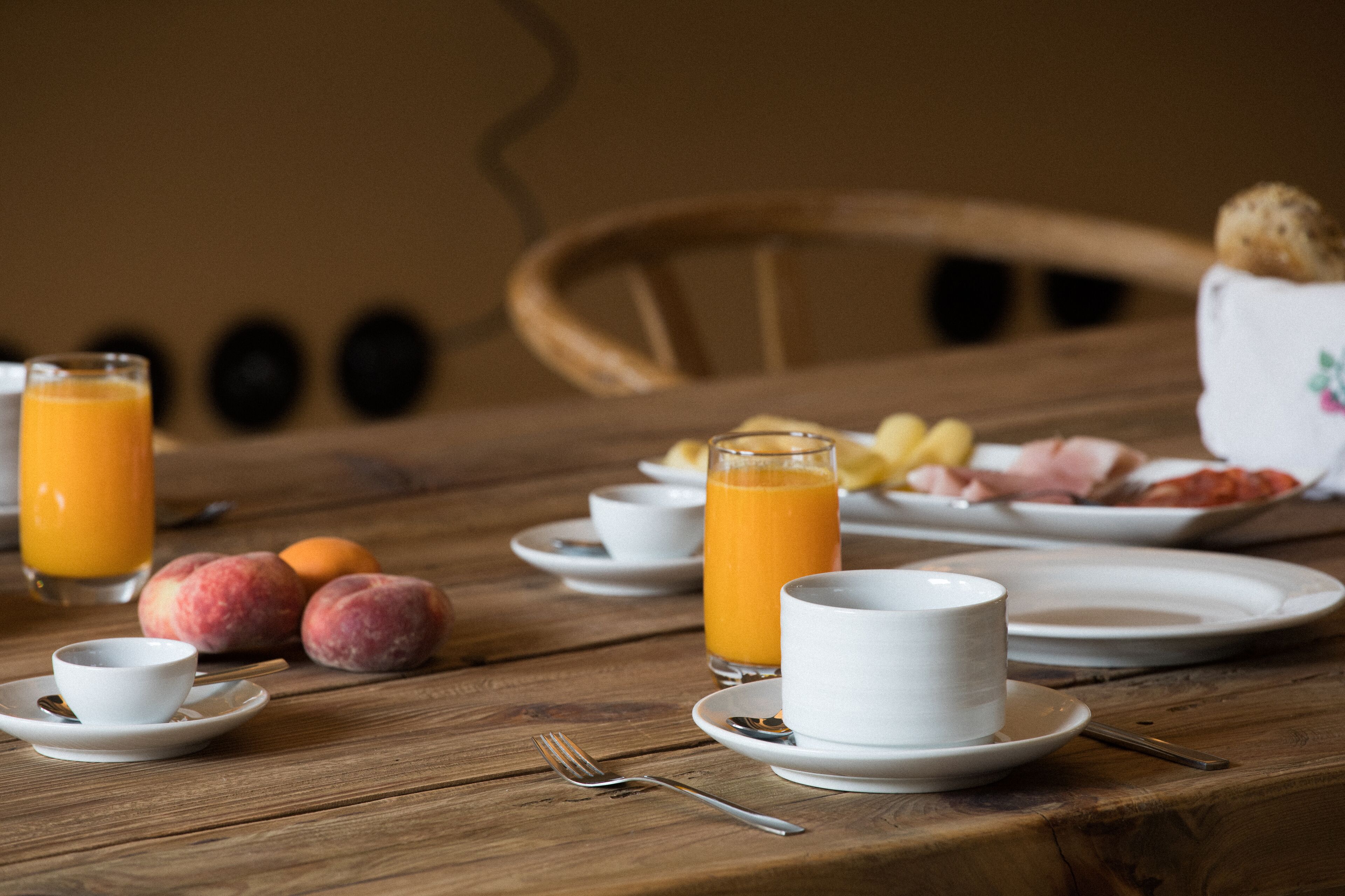A wooden table with breakfast items including a glass of orange juice, a cup, plates with food, and a fork.
