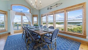 A dining area with a large table, chairs, and a view of the landscape. - Soundside Dog Friendly Home w/ Private Pool, Hot Tub, Elevator, and Game Room (Avon)