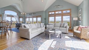 A spacious living room with a high ceiling, large windows, and a view of the landscape. - Soundside Dog Friendly Home w/ Private Pool, Hot Tub, Elevator, and Game Room (Avon)