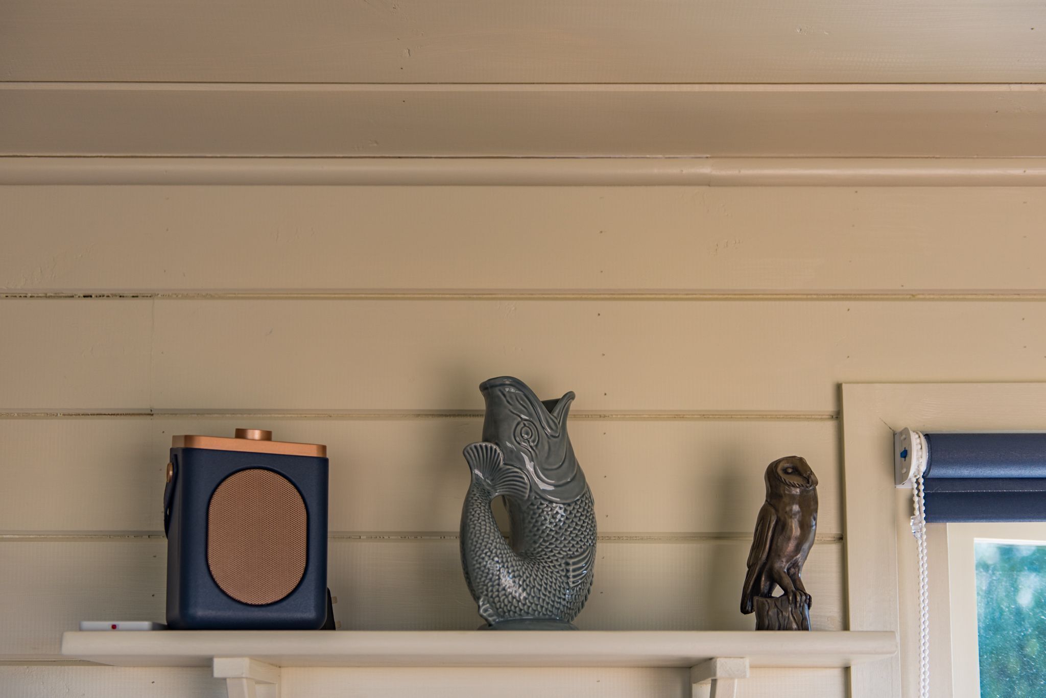 Een plank met een speaker, een vaas in de vorm van een vis en een beeldje van een uil.