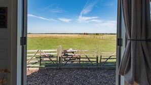 Blick aus einem Zimmer mit Holzzaun und Picknicktisch im Freien, bewölkter Himmel und Kiesfläche im Vordergrund.
