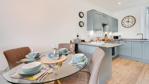 Une cuisine moderne avec des meubles bleus, un îlot central rond et un coin repas comprenant une table en verre et des chaises marron.