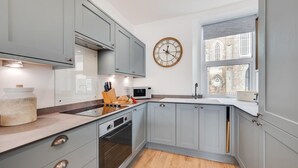 Une cuisine moderne avec des meubles gris, un four encastré, un four à micro-ondes et une horloge en bois accrochée au mur.
