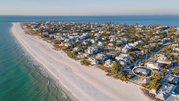 An aerial view of a coastal residential area with houses along the beach and a clear view of the ocean.