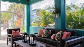 A cozy seating area with a sofa and chairs, a coffee table, and a view of palm trees and houses through large windows.