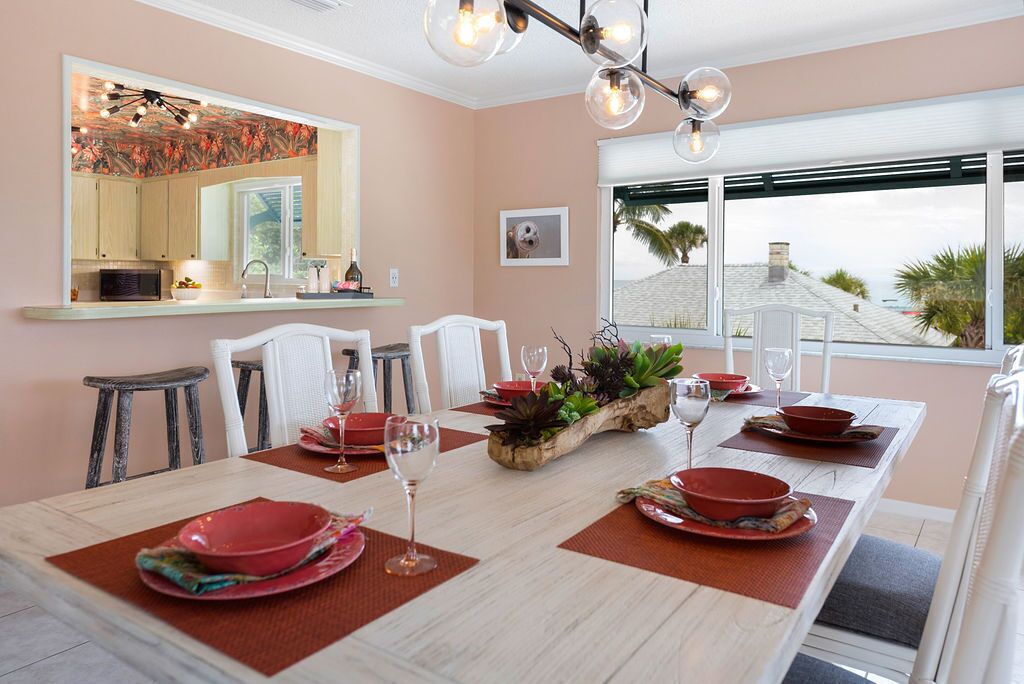 A dining area with a long table set for six, white chairs, and a modern chandelier.