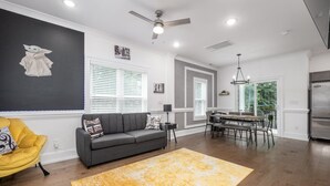 Un salon moderne avec un canapé gris, un fauteuil jaune et un coin repas comprenant une table et des chaises.