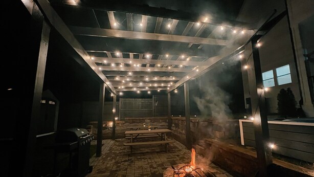 Une terrasse extérieure dotée d’un foyer, de bancs en bois et de guirlandes lumineuses.