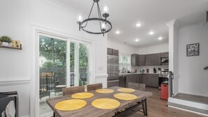 Une cuisine moderne dotée d’appareils électroménagers en acier inoxydable, un coin repas avec une table en bois et des sets de table jaunes, et une porte-fenêtre coulissante donnant sur un balcon.