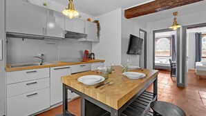 Eine moderne Küche mit weißen Schränken, einem Holzespeisetisch für vier Personen und einem an der Wand montierten Fernseher.