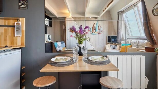 Une cuisine moderne avec une table en bois dressée pour deux personnes, un réfrigérateur et une fenêtre avec des rideaux.