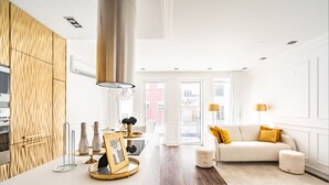 Ein modernes Wohnzimmer mit einem weißen Sofa, einem Couchtisch und einer Küchenzeile mit Holzausbau und einer weißen Arbeitsplatte.