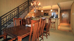 Un vaste espace dédié à la salle à manger, avec une grande table et des chaises en bois, un lustre et une cuisine en arrière-plan.