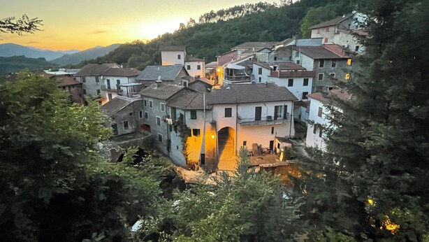A hillside village with traditional architecture, including stone buildings with sloped roofs and a central building with a prominent archway.