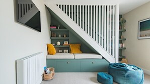 Un interior moderno con una zona de estar integrada debajo de una escalera, un radiador, una cesta y un sillón de peluche azul.
