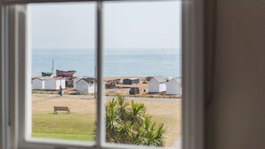 Vista desde una ventana a una zona de playa con un camino de arena, un banco y varios edificios pequeños.