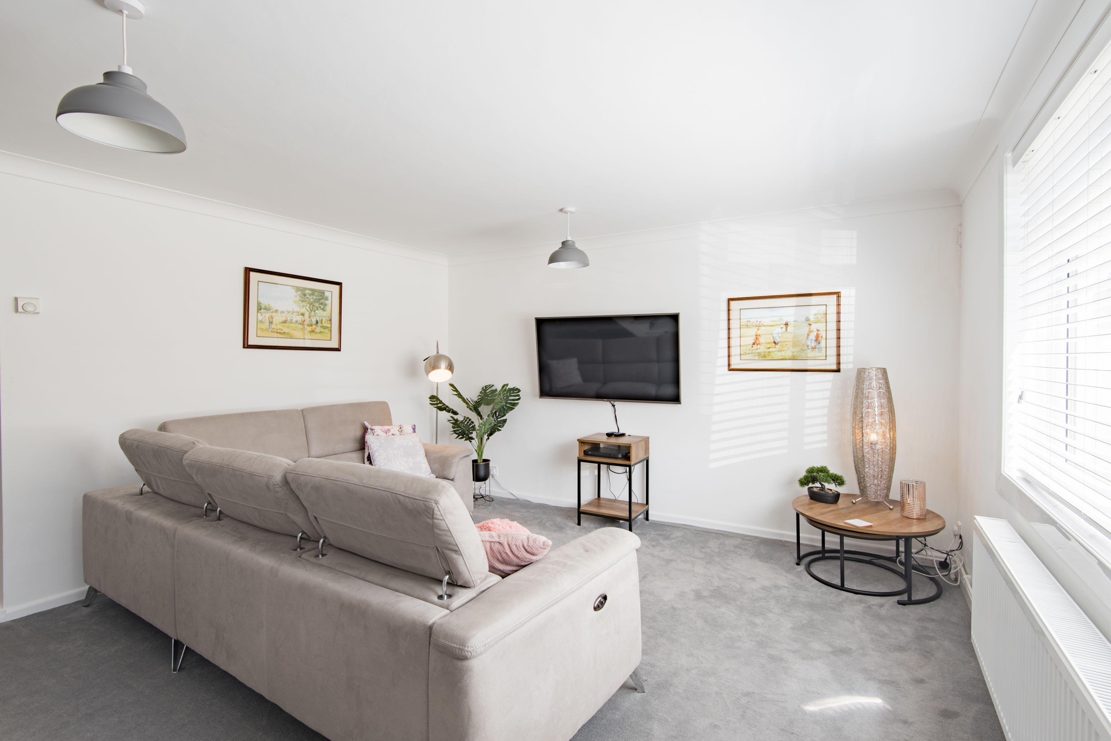 A modern living room with a beige sofa, a flat-screen TV, and two framed pictures on the walls.