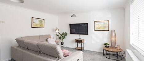 A modern living room with a beige sofa, a flat-screen TV, and two framed pictures on the walls.