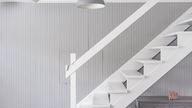 Een moderne trap met witte leuningen en een grijze hanglamp.
