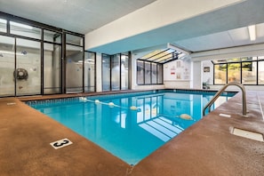 Una piscina interna con pareti di vetro trasparenti, acqua blu e una scala in metallo.