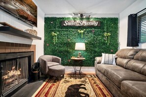 Un salon avec une cheminée, un canapé, un fauteuil, un tapis et un mur orné de plantes et d’une inscription indiquant « Suite Serenity ».