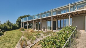 A modern house with a glass extension, a garden with various plants, and a clear blue sky.