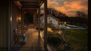 A covered outdoor area with benches and a small building, likely a guest house or service area, with a pool in the background.