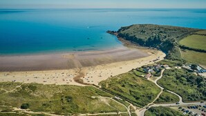 An aerial view of a coastal area with a beach, a small settlement with houses, and a road leading to the beach.