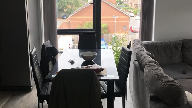 Una sala de estar moderna con comedor, un sofá y vistas a una zona residencial a través de ventanas amplias.