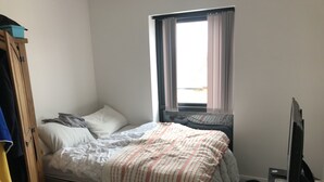 Un dormitorio con cama, ventana con cortinas, armario y televisor.