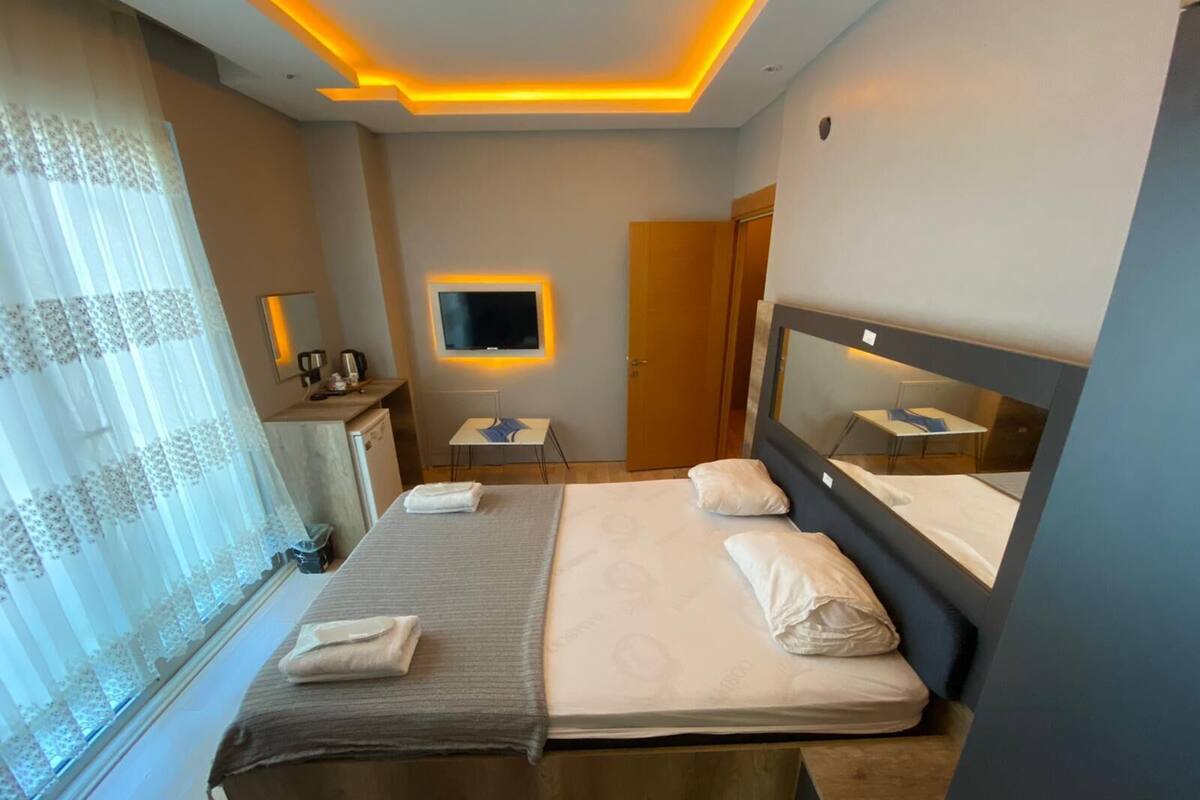 Quarto de hotel moderno com cama, mesa de cabeceira e televisão na parede.