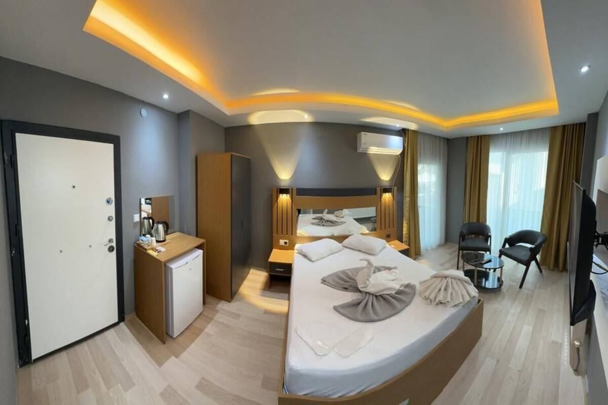 Quarto de hotel moderno com uma cama grande, mesas de cabeceira, escrivaninha, guarda-roupa e televisão.