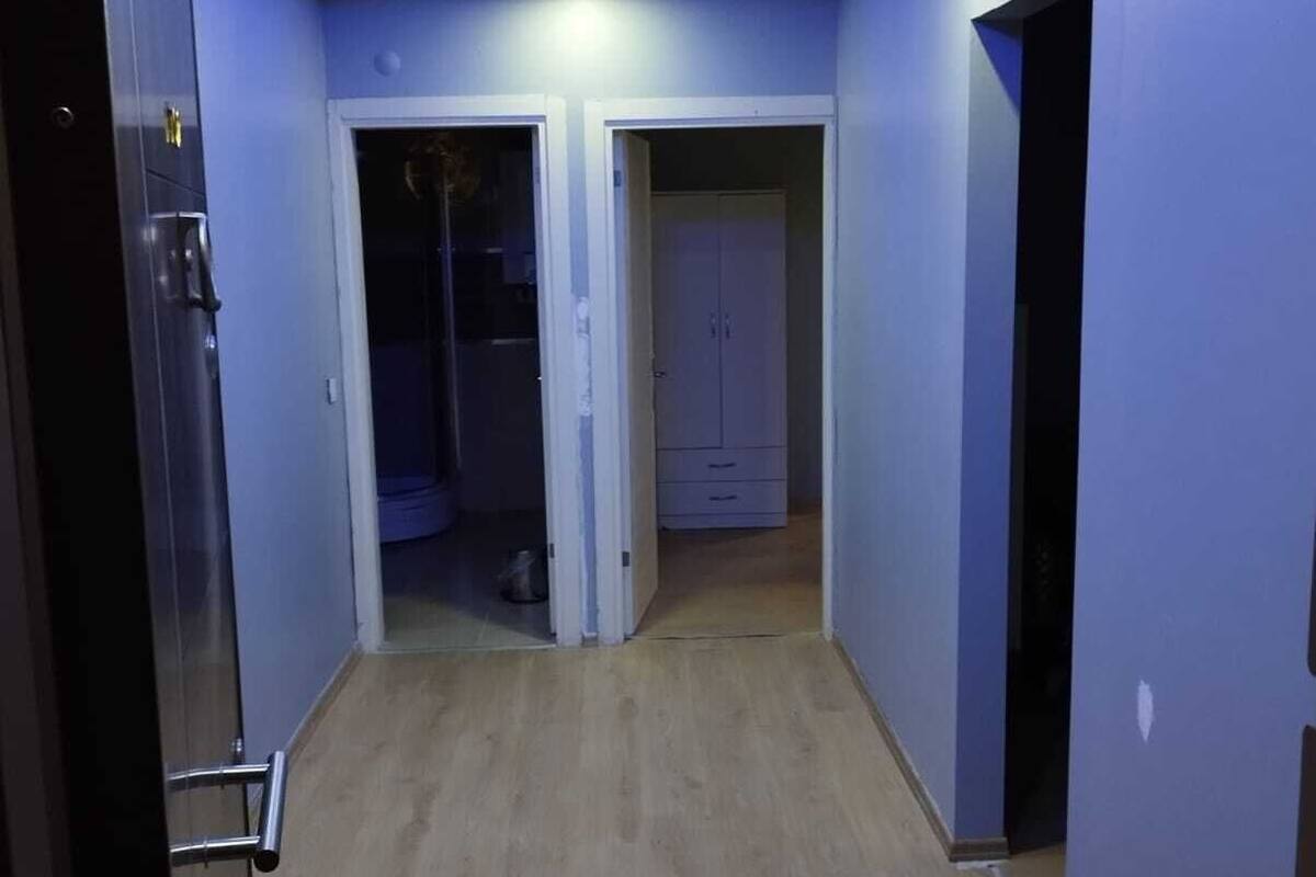 Um corredor com piso de madeira, teto com iluminação embutida e duas portas dando acesso a quartos.