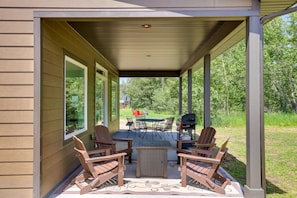 Un patio techado con mesa y sillas, una parrilla y vistas a un espacio verde.