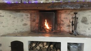 A fireplace with a clear glass front, a stone wall, and a wooden mantel.