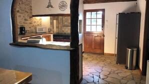 A rustic kitchen with stone flooring, a wooden door, and a built-in stove.
