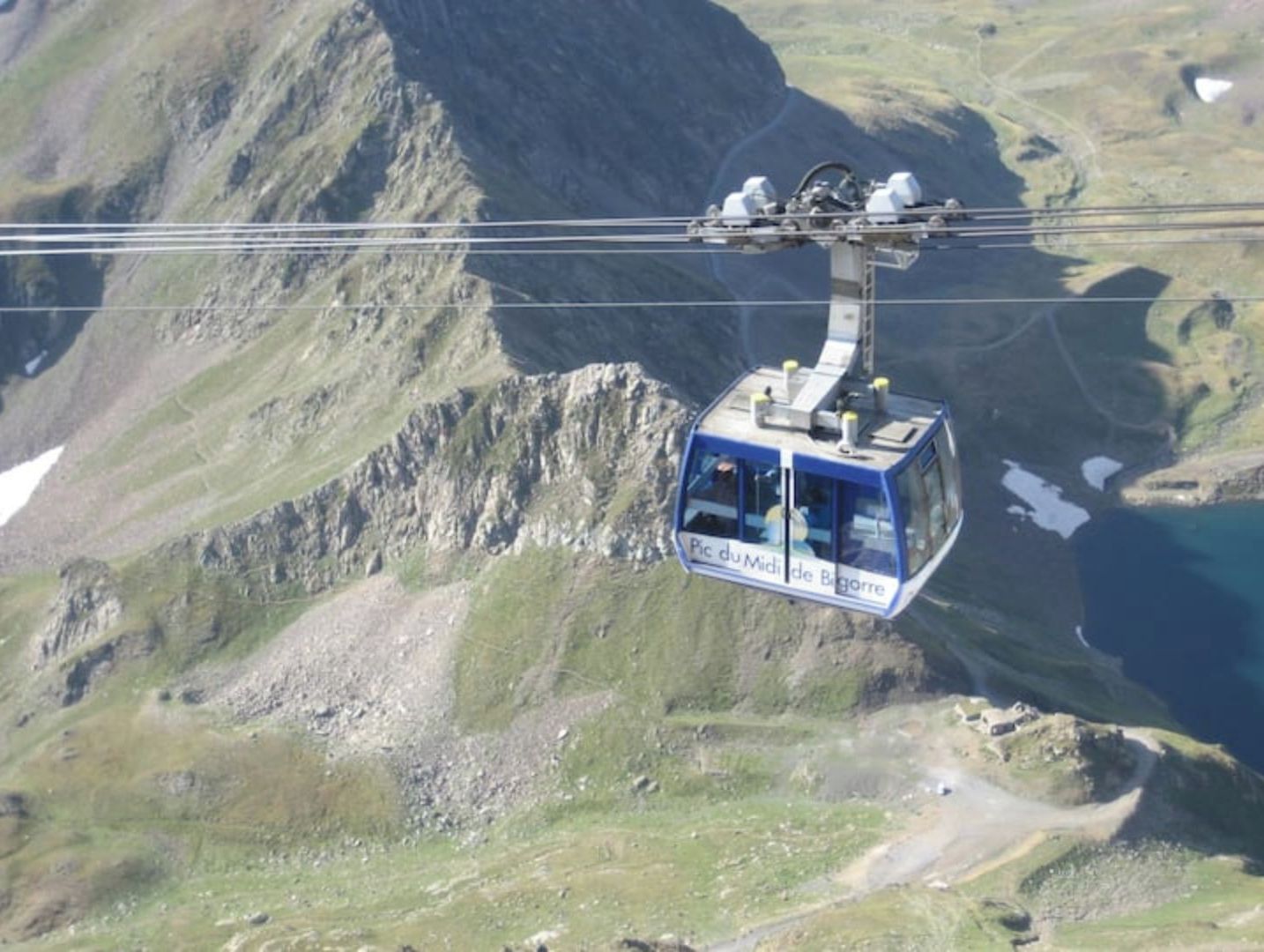 Eine Standseilbahn mit einem Schild, das "Pic du Midi de Bigorre" zeigt, schwebt über einer gebirgigen Landschaft.
