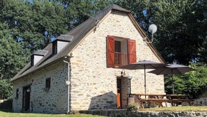 A stone building with a sloped roof, wooden shutters, and a satellite dish.