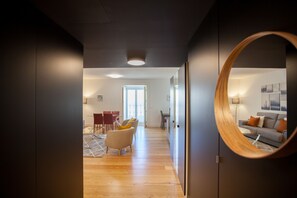 Un soggiorno moderno con pavimento in legno, uno specchio rotondo e vista su un'altra stanza attraverso una porta.