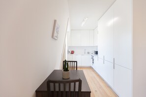 A modern kitchen with white cabinets, a wooden dining table with a cactus, and a small coffee machine.