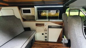 Interior compacto de una furgoneta con kitchenette, una televisión pequeña y una zona de estar acolchada.
