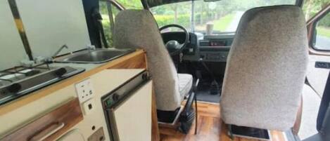 A compact RV interior with a kitchenette, seating area, and a small storage unit.
