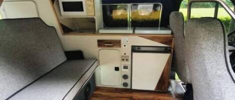 A compact van interior with a kitchenette, a small TV, and a cushioned seating area.