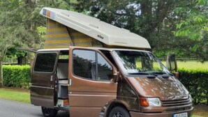 Una caravana marrón con un toldo grande y blanco a rayas en el techo.