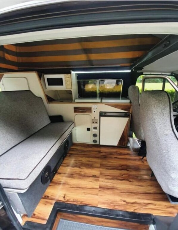 A compact van interior with a kitchenette, a small TV, and a cushioned seating area.
