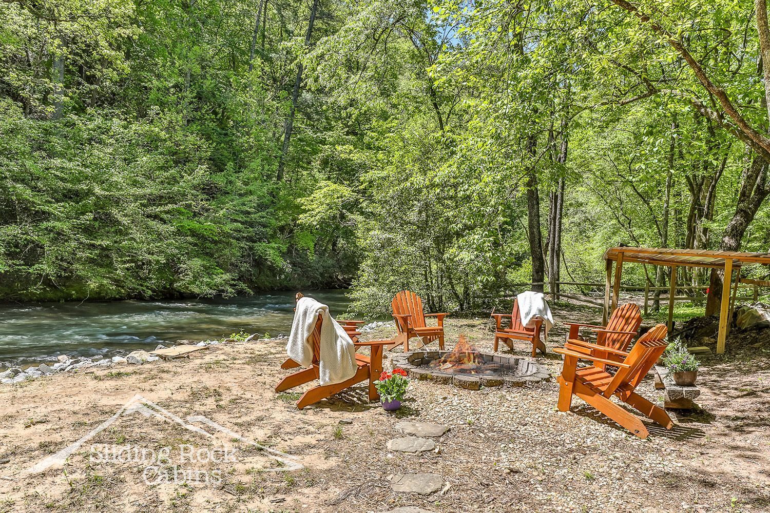 Ein Flussufer-Campingplatz mit Holzsesseln und einer Feuerstelle.