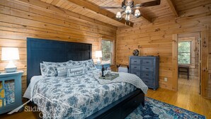 A wooden cabin bedroom with a bed, nightstand, dresser, and a ceiling fan. - Trout Haven | No Pet Fees | Sleeps 6 | Creekfront | Outdoor pavillion w/ TV (Ellijay)