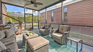 A covered outdoor seating area with wicker furniture, a ceiling fan, and a view of a red house. - Everglades City Cabin: Dock & Heated Pool! (Everglades City)