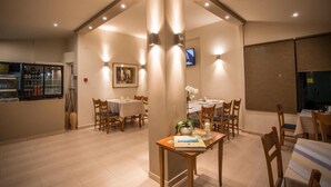 Un espace repas avec des tables et des chaises, un téléviseur fixé au mur et un réfrigérateur contenant des boissons.